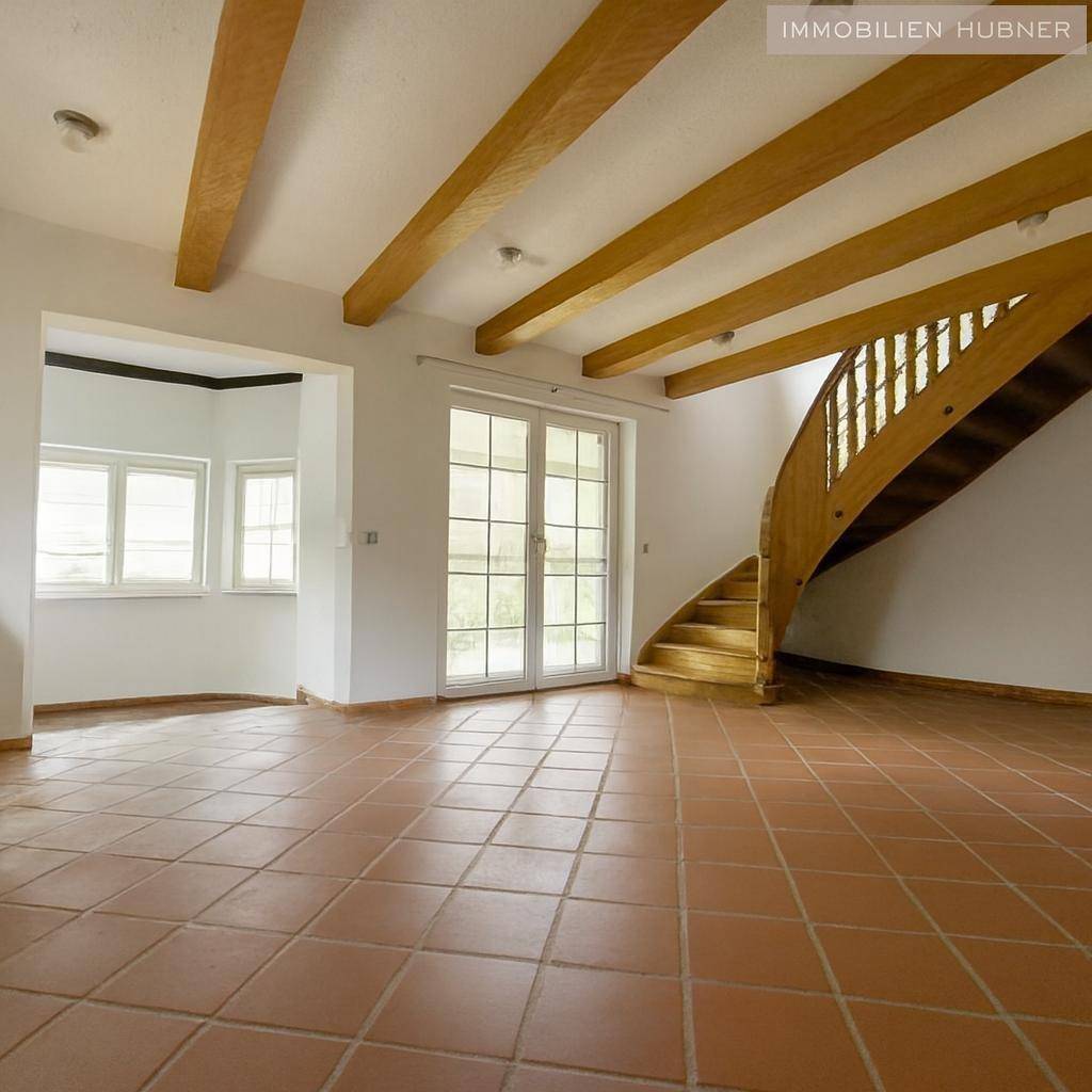 Geräumiges Wohnzimmer mit Terrakottafliesen, Holzbalken und offener Holztreppe.