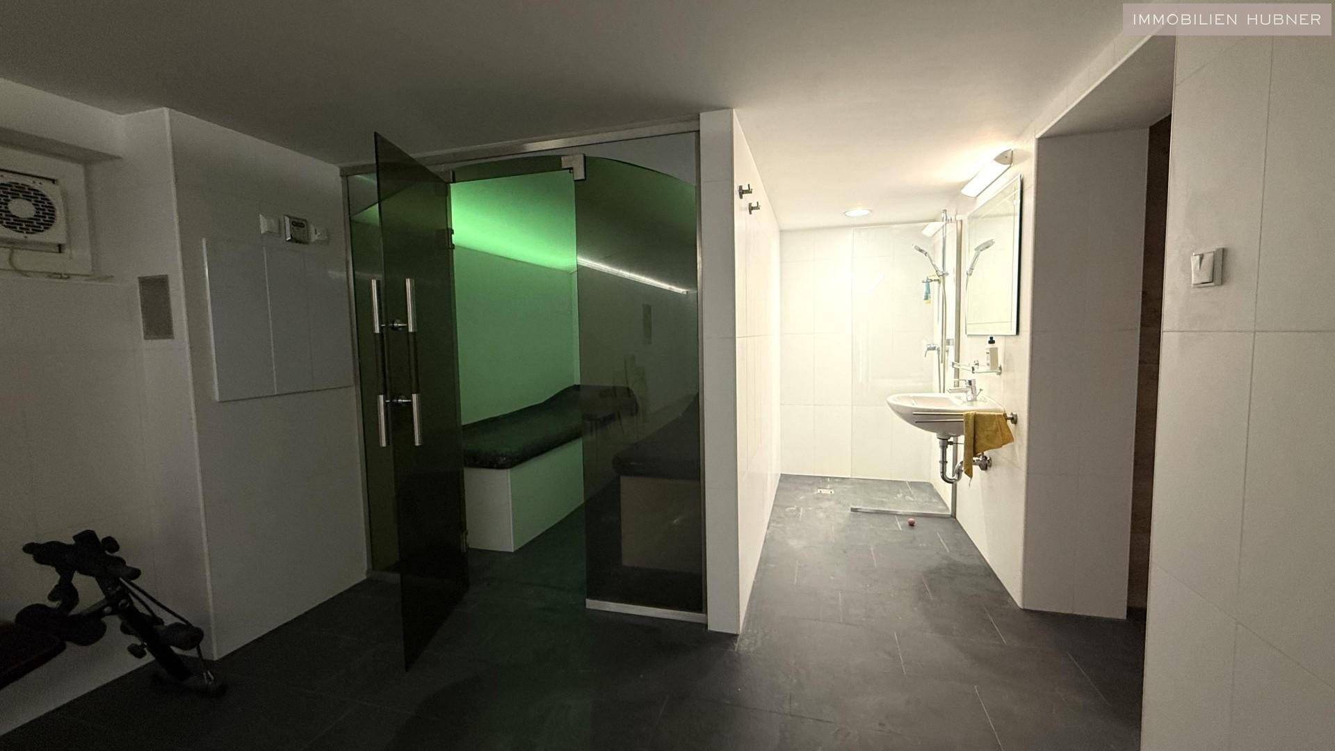 Wellnessbereich mit Dusche, Waschbecken und Zugang zu einer Dampfsauna oder Infrarotkabine.