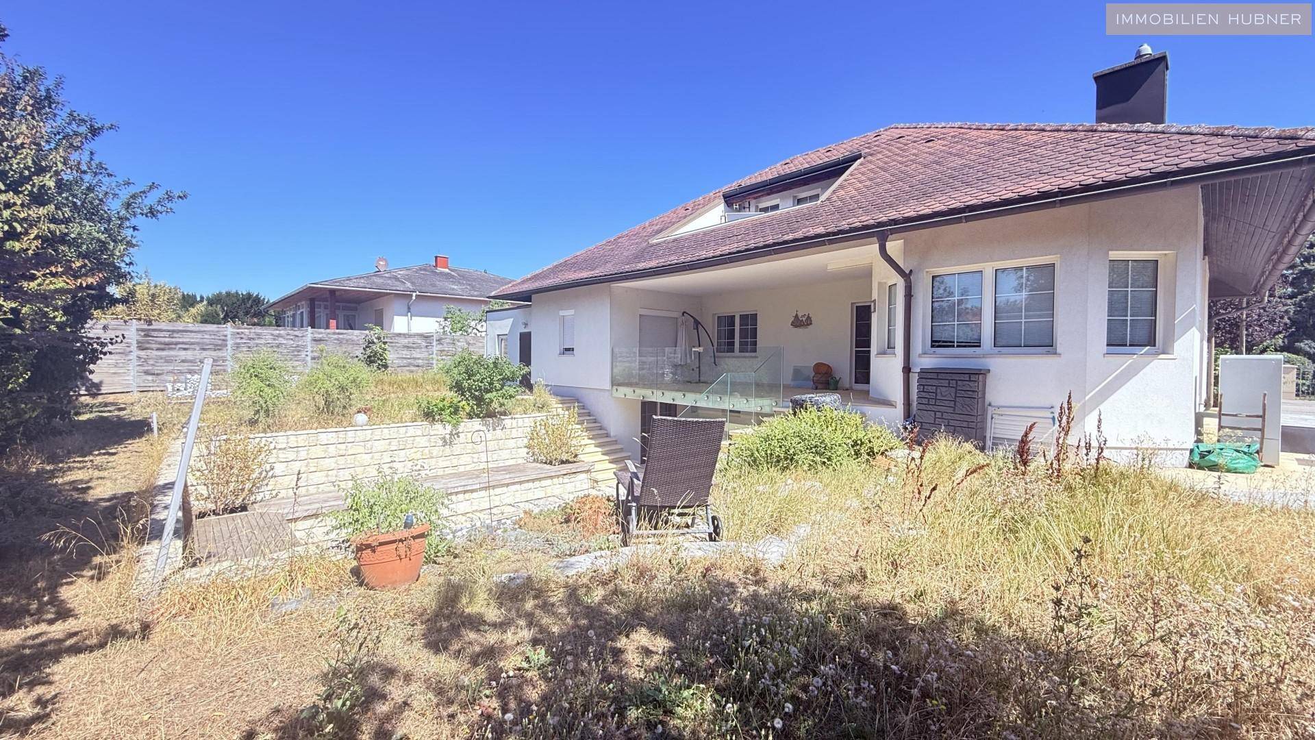 Rückansicht des Hauses mit Garten, Terrasse und Treppenabgang unter klarem Himmel.