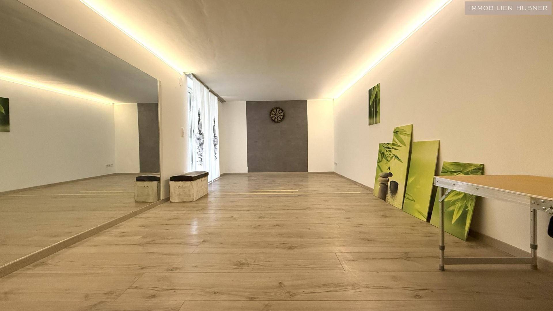 Großer Raum mit Spiegelwänden, Laminatboden und indirekter Beleuchtung, ideal für Sport.