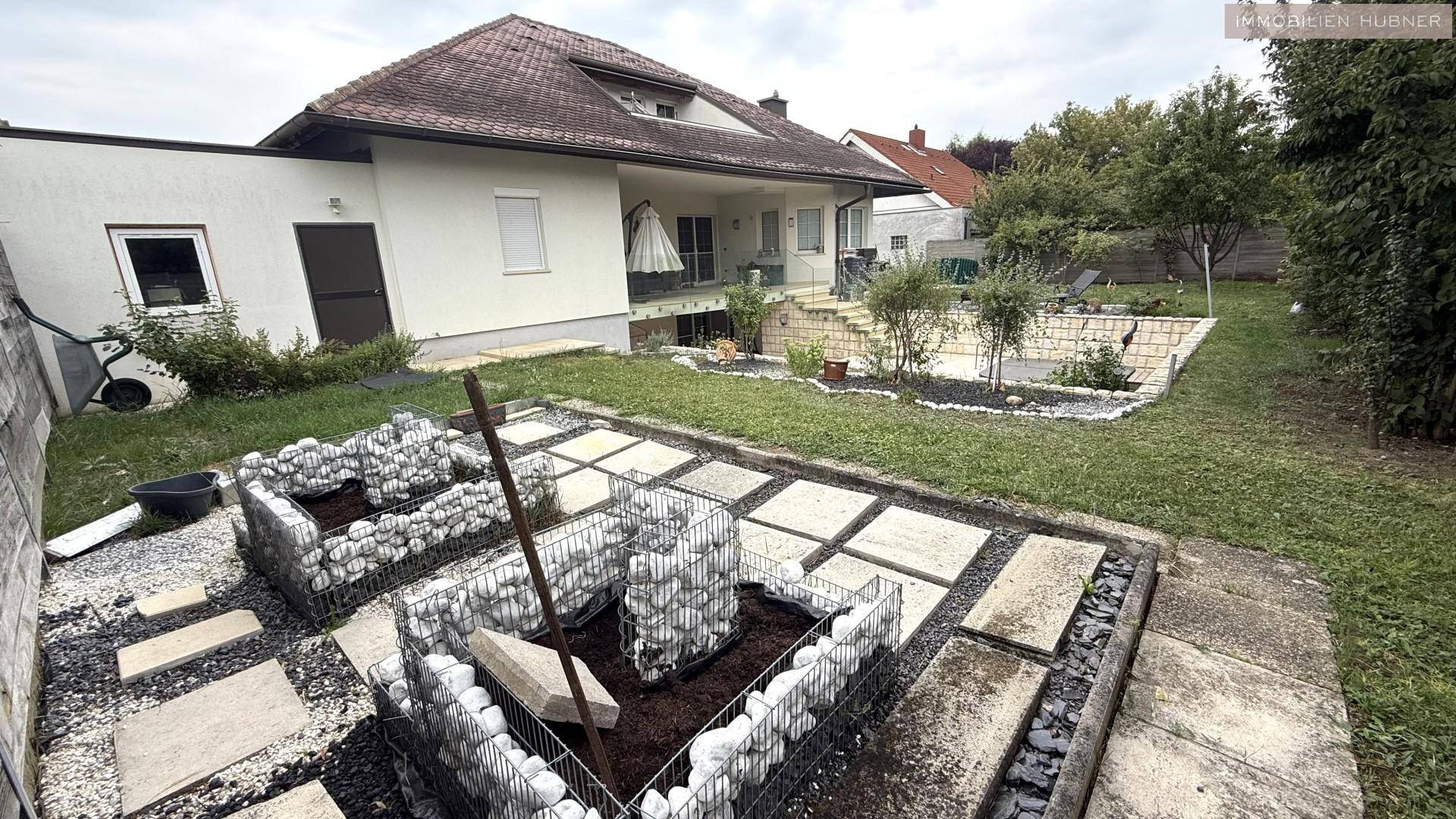 Gartenbereich mit Hochbeeten und Blick auf die Rückseite des Hauses an einem bewölkten Tag.