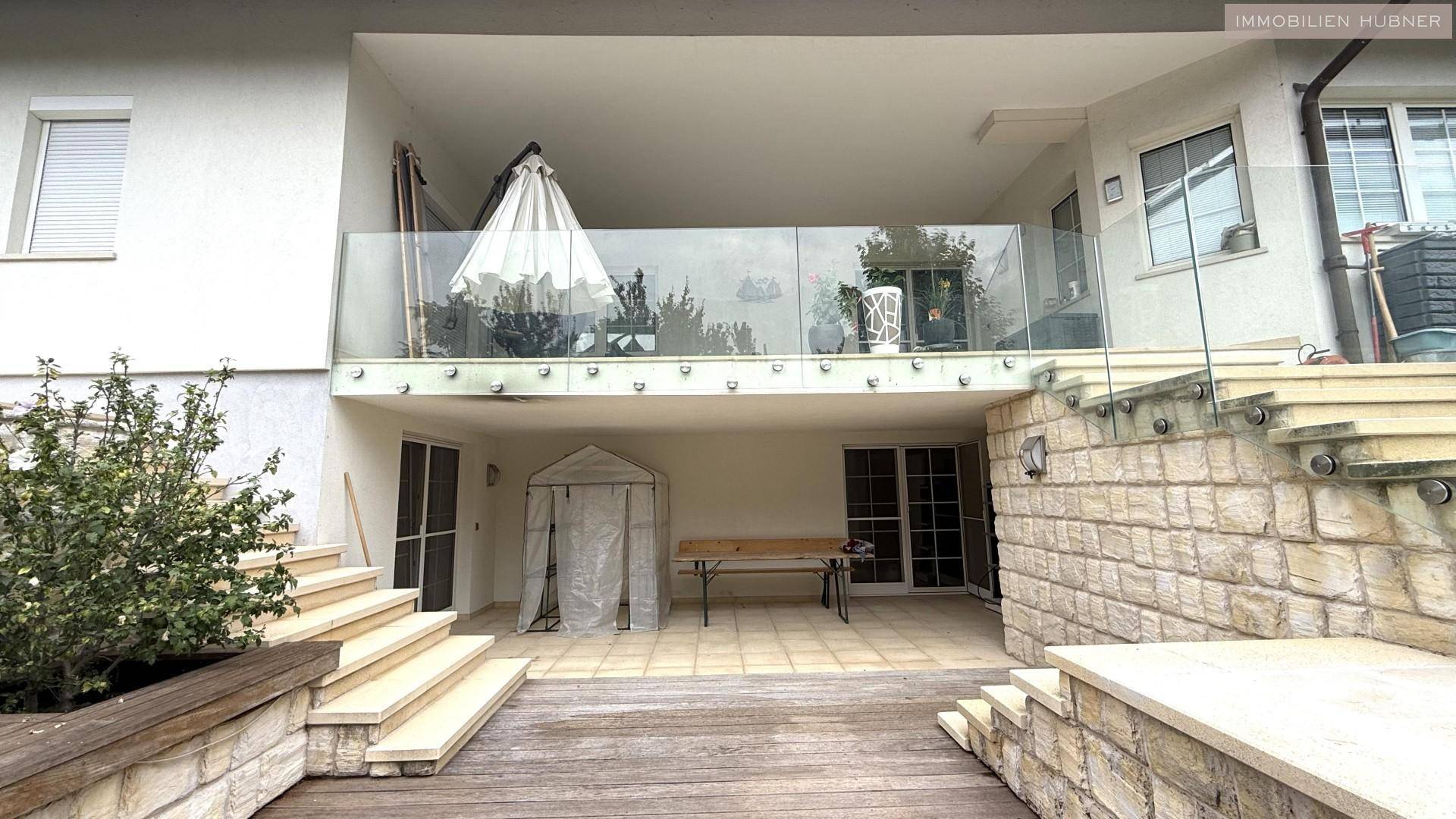 Überdachte Terrasse mit Glasgeländer und Treppen zum unteren Gartenbereich.