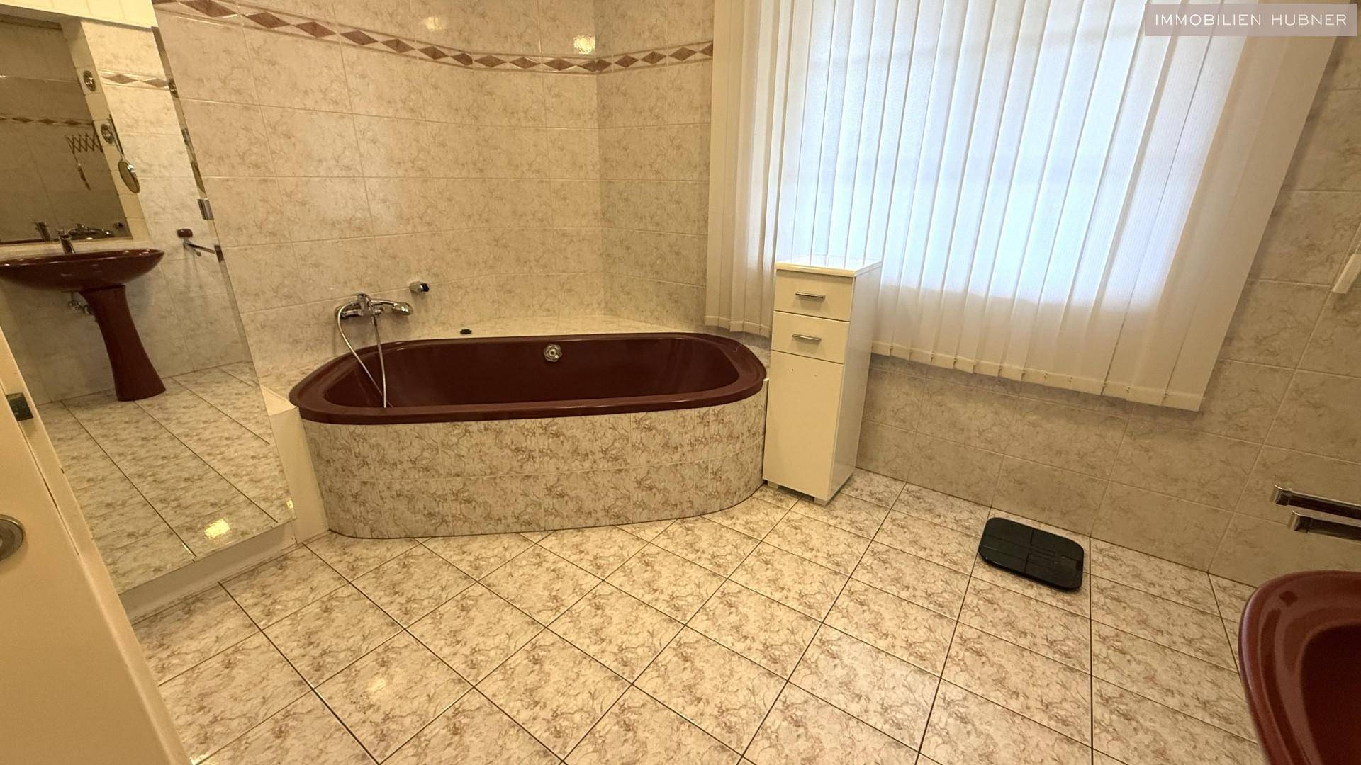 Badezimmer mit Eckbadewanne, Waschbecken und gemusterten Fliesen im 80er-Jahre-Stil.