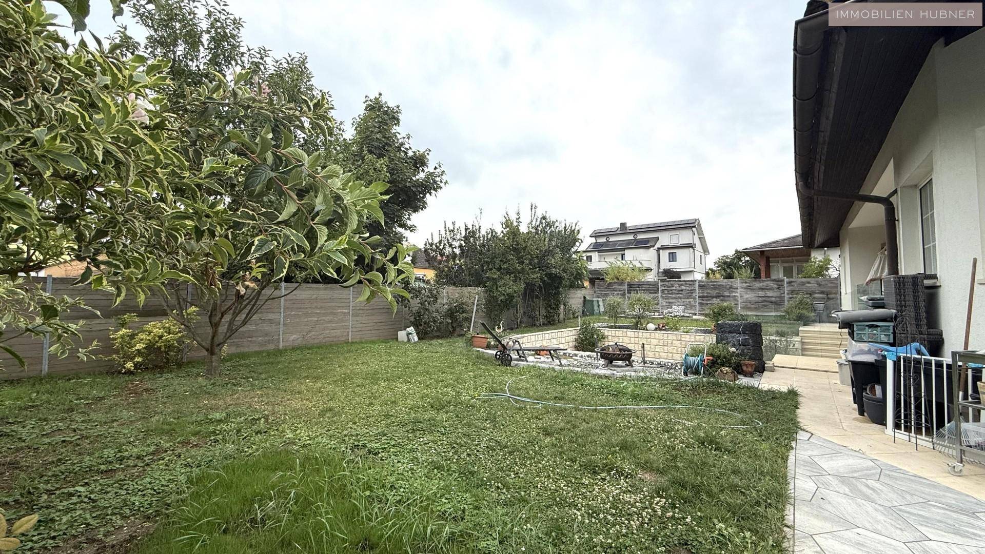Gepflegter Gartenbereich mit Rasenfläche, Bäumen und seitlichem Zugang zum Haus.