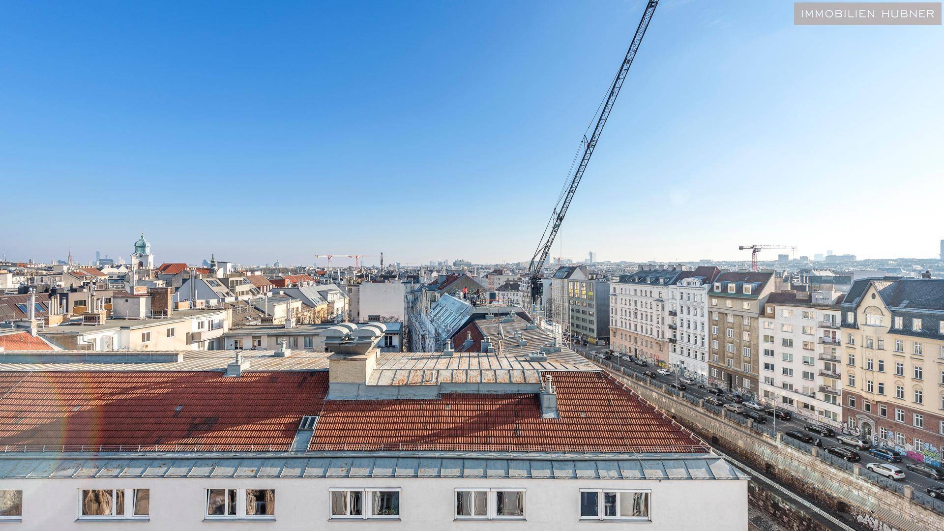 Panoramablick über die städtische Skyline mit Dächern und einem Baukran am Horizont.