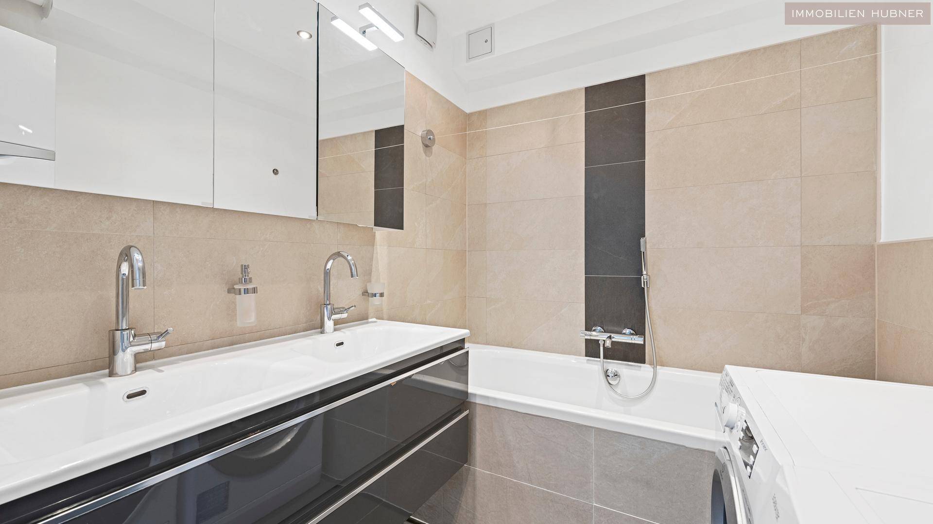 Modernes Badezimmer mit Doppelwaschbecken, Badewanne und beigefarbenen Fliesen.