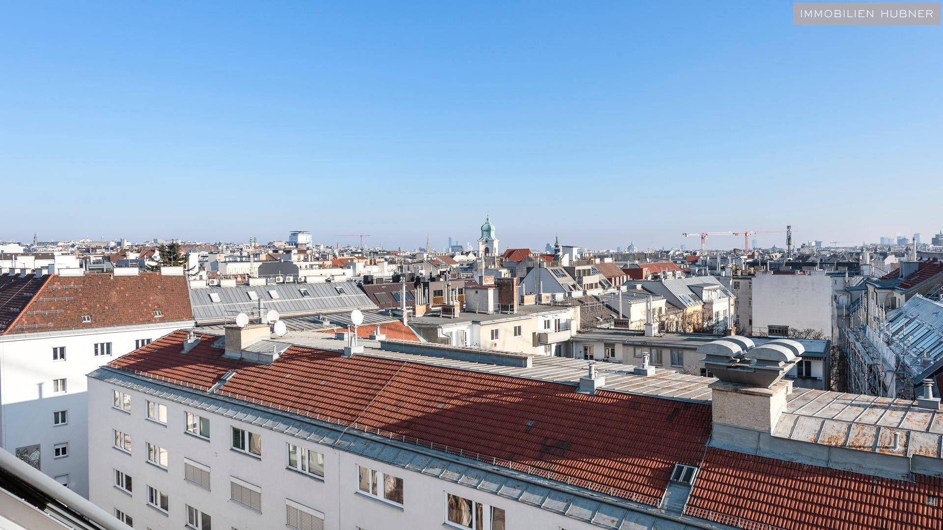 Weitläufiger Blick über die Dächer der Stadt mit historischer Architektur und blauem Himmel.