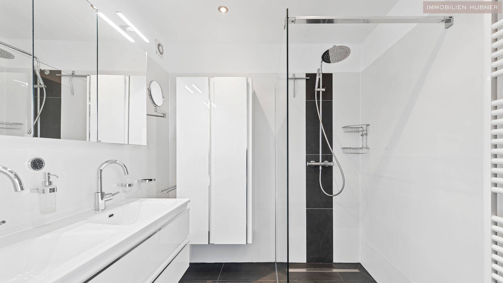 Modernes Badezimmer mit großer begehbarer Dusche, Doppelwaschbecken und weißen Fliesen.