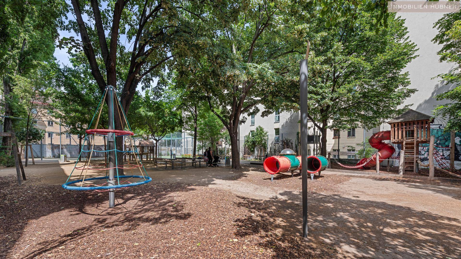 Öffentlicher Spielplatz mit verschiedenen Spielgeräten wie Rutschen und Kletterstrukturen, umgeben von Bäumen.