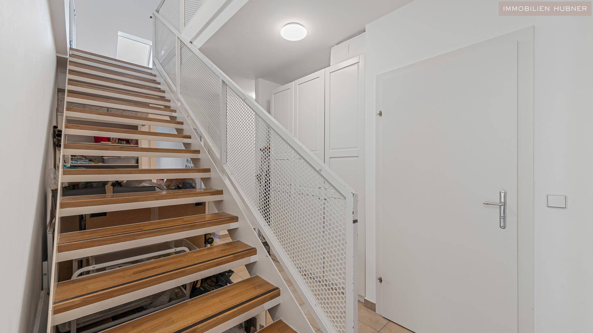 Heller Treppenaufgang mit Holzstufen und modernem weißen Metallgeländer, führt zu den oberen Etagen.
