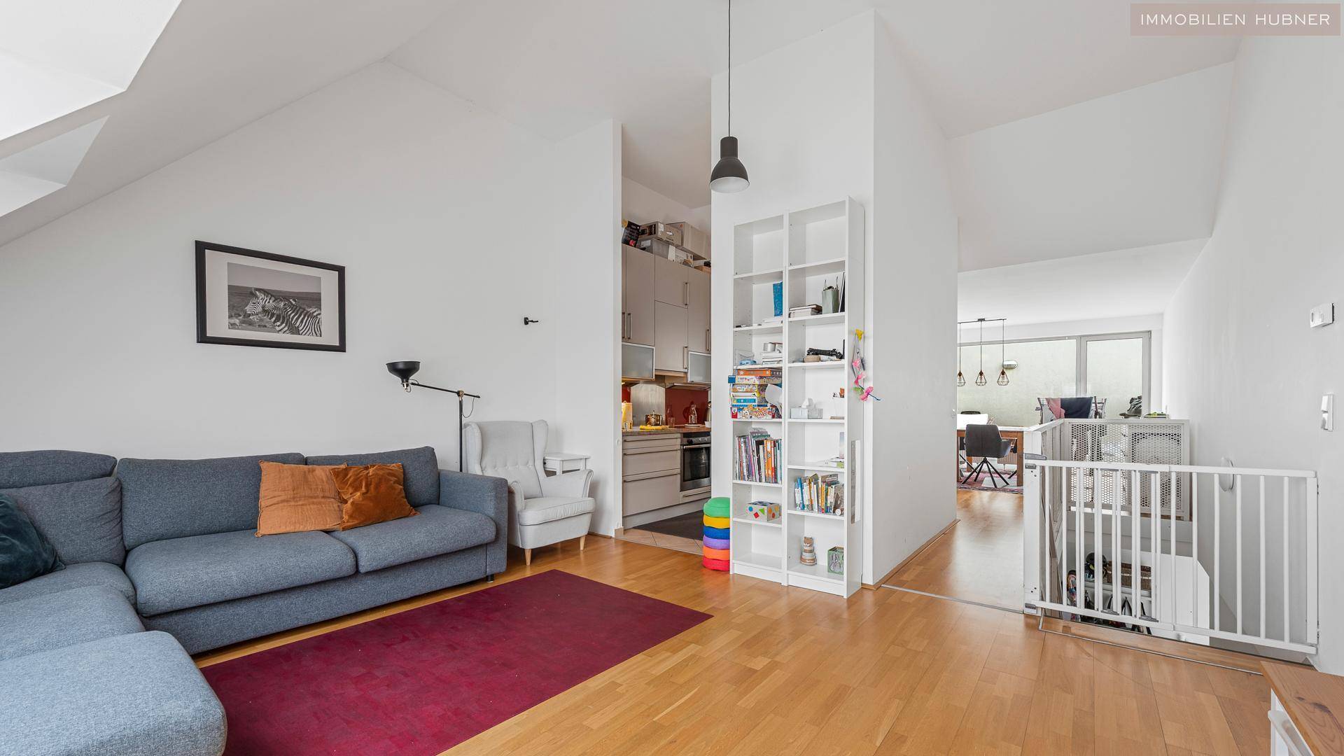 Offener Wohnbereich mit Sofa, Bücherregal und Blick auf die Küche sowie eine Treppe mit Kindersicherung.