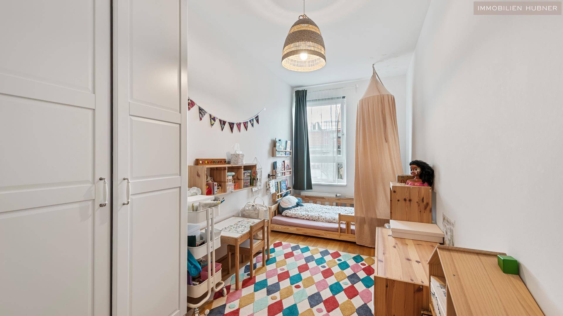 Helles Kinderzimmer mit Holzbett, bunten Teppich und kindgerechter Einrichtung, ideal für ein Kleinkind.