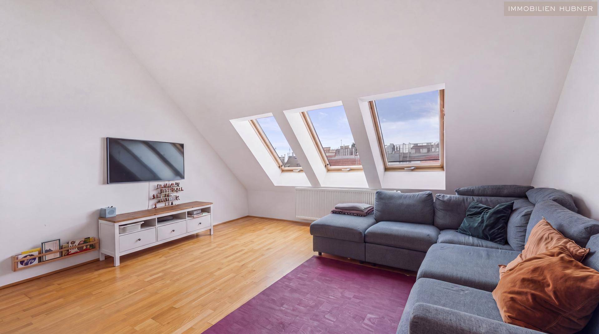 Gemütliches Wohnzimmer im Dachgeschoss mit Schrägdach, drei Dachfenstern und einem großen Ecksofa.