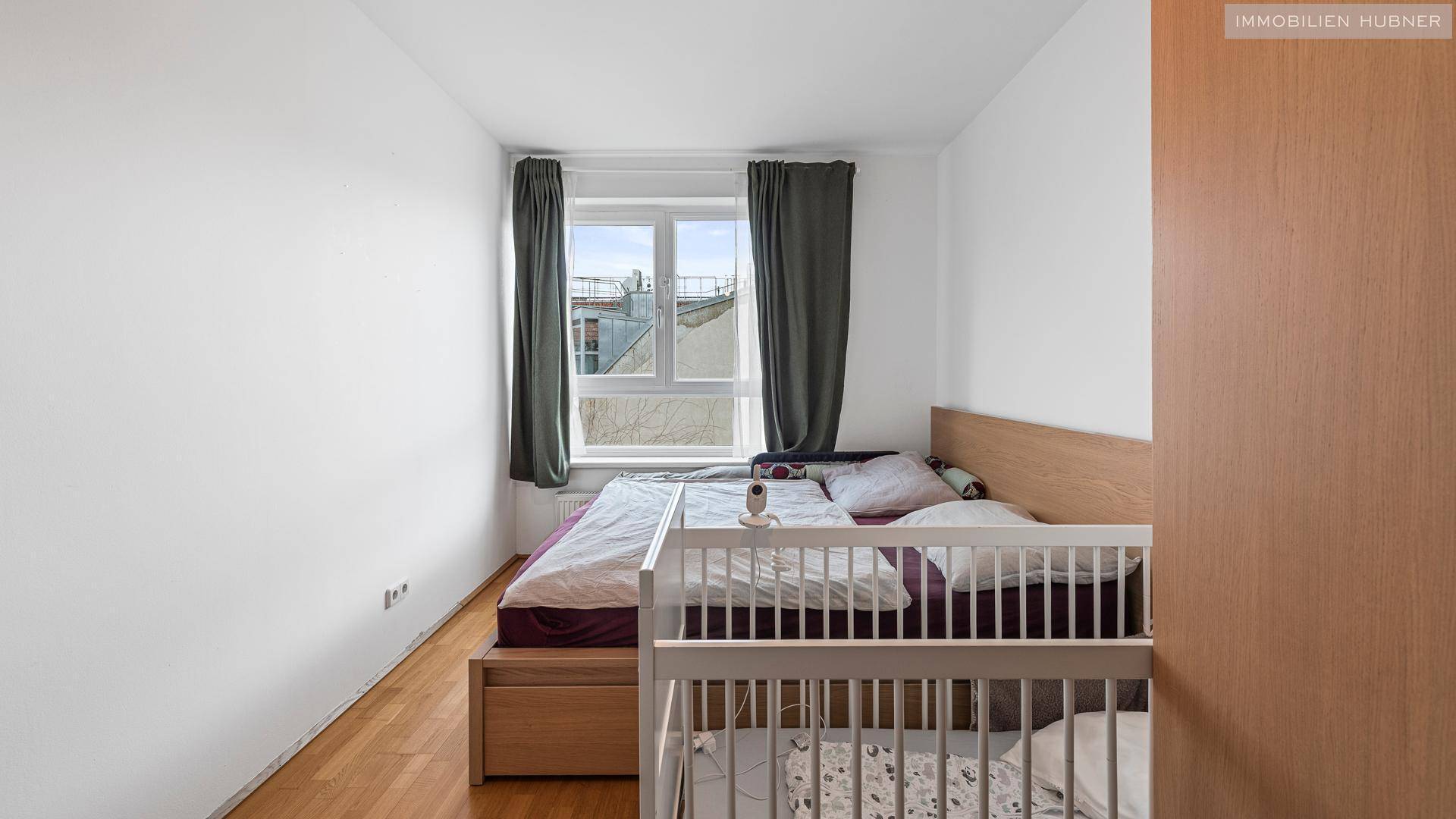 Schlafzimmer mit Doppelbett, Babybett und Fenster, bietet eine ruhige und helle Atmosphäre.