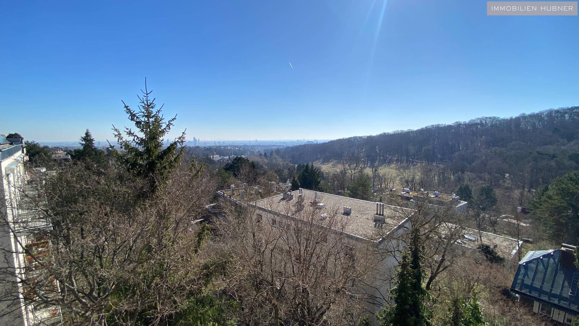 Weitläufiger Panoramablick über grüne Hügel und die Stadt in der Ferne unter strahlend blauem Himmel.