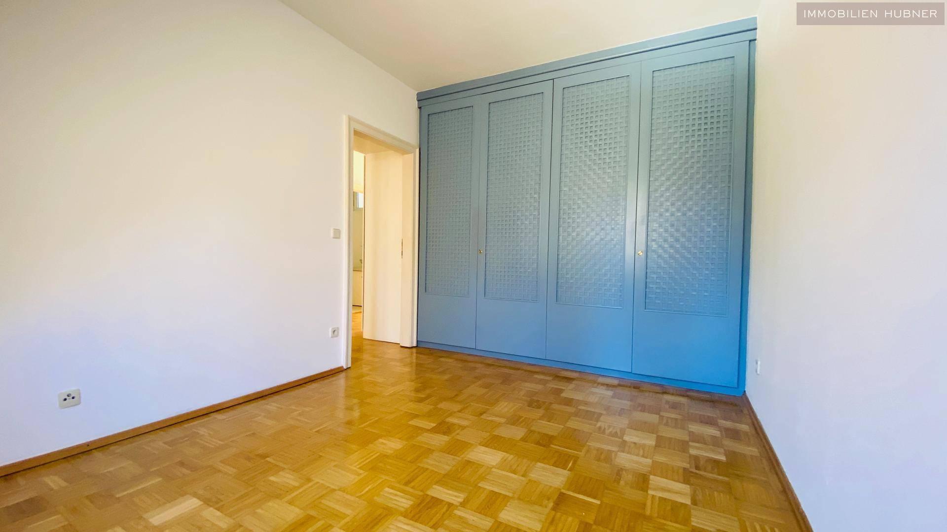 Schlafzimmer mit Parkettboden und einem großen, blauen Einbauschrank, der viel Stauraum bietet.