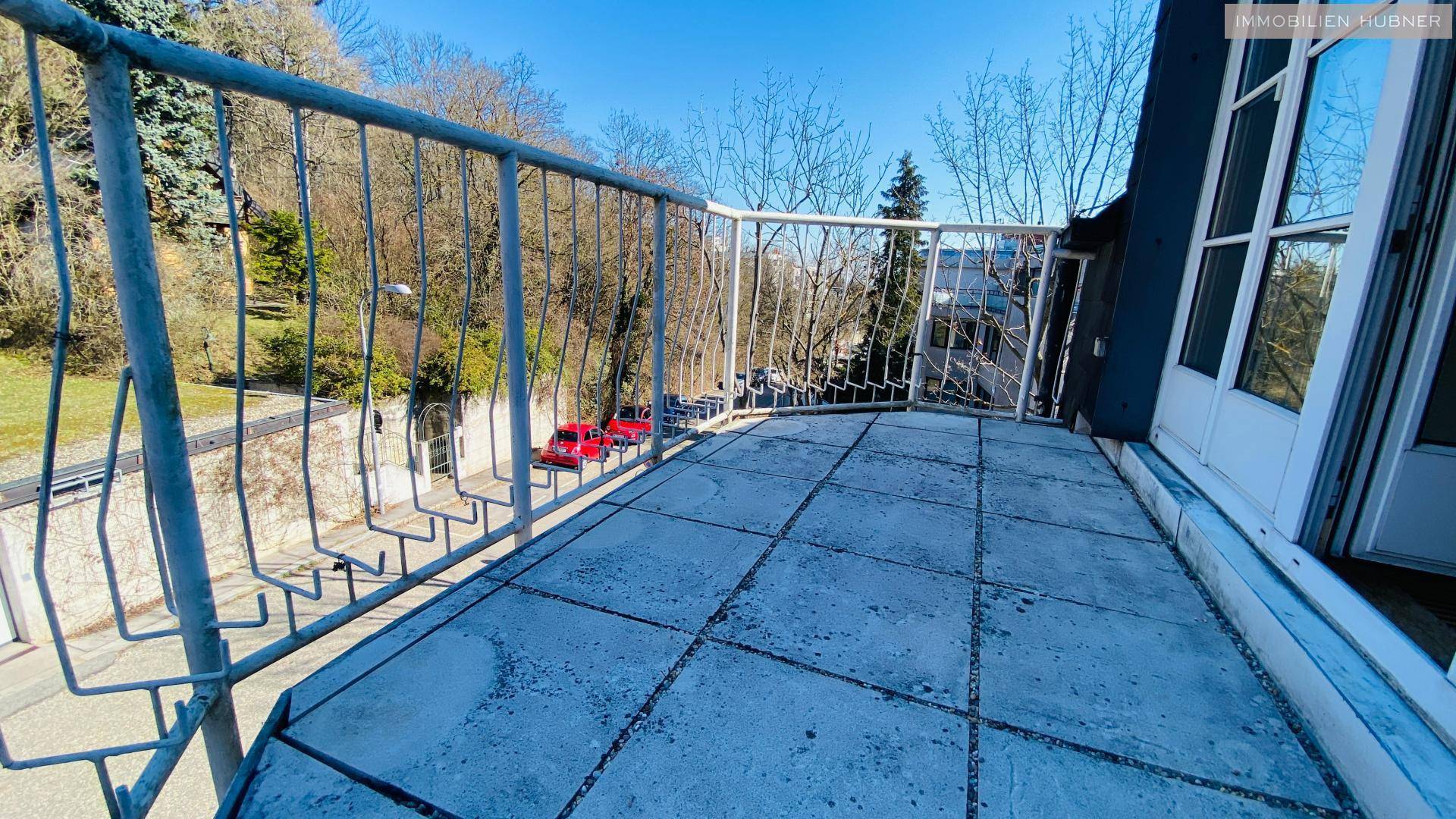 Kleiner Balkon mit Fliesenboden und Metallgeländer, bietet Blick auf die Straße und Bäume.