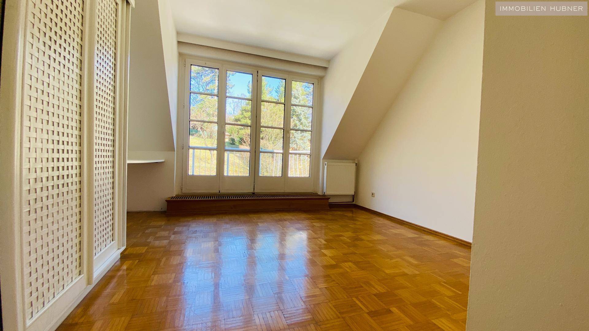 Helles Zimmer im Dachgeschoss mit Parkettboden, großen Fenstern und charakteristischer Dachschräge.