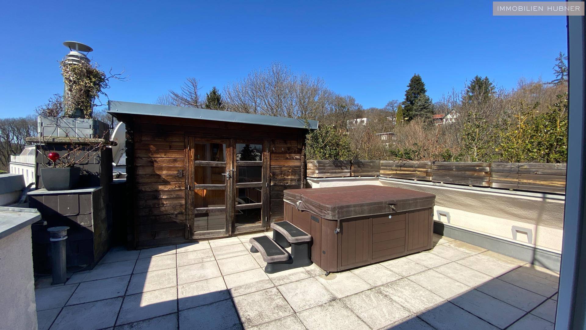 Große Dachterrasse mit Whirlpool, einer Holzhütte und weitem Blick ins Grüne.