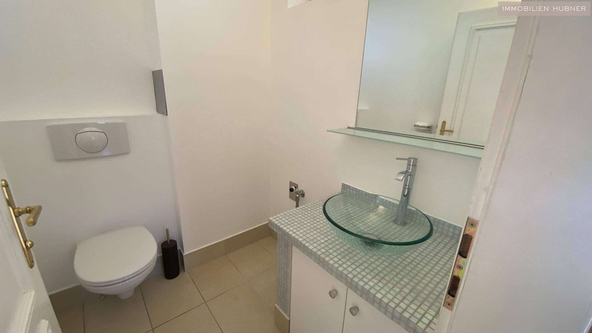 Modernes Gäste-WC mit wandhängender Toilette, einem Glaswaschbecken und Fliesenboden.