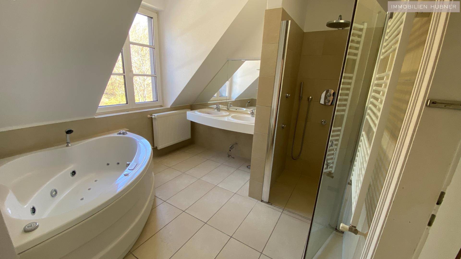 Geräumiges Badezimmer mit Whirlpool-Badewanne, Doppelsink, Dusche und Fenster in der Dachschräge.