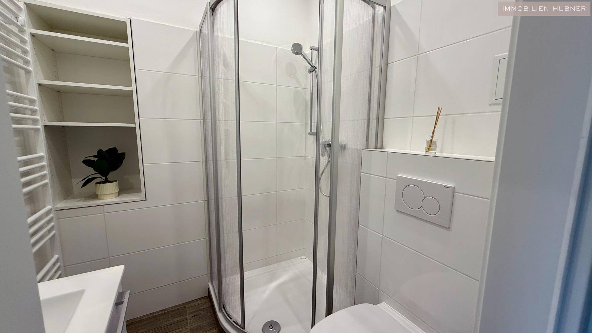 Ansicht des Badezimmers mit Duschkabine, WC und praktischen Wandregalen.