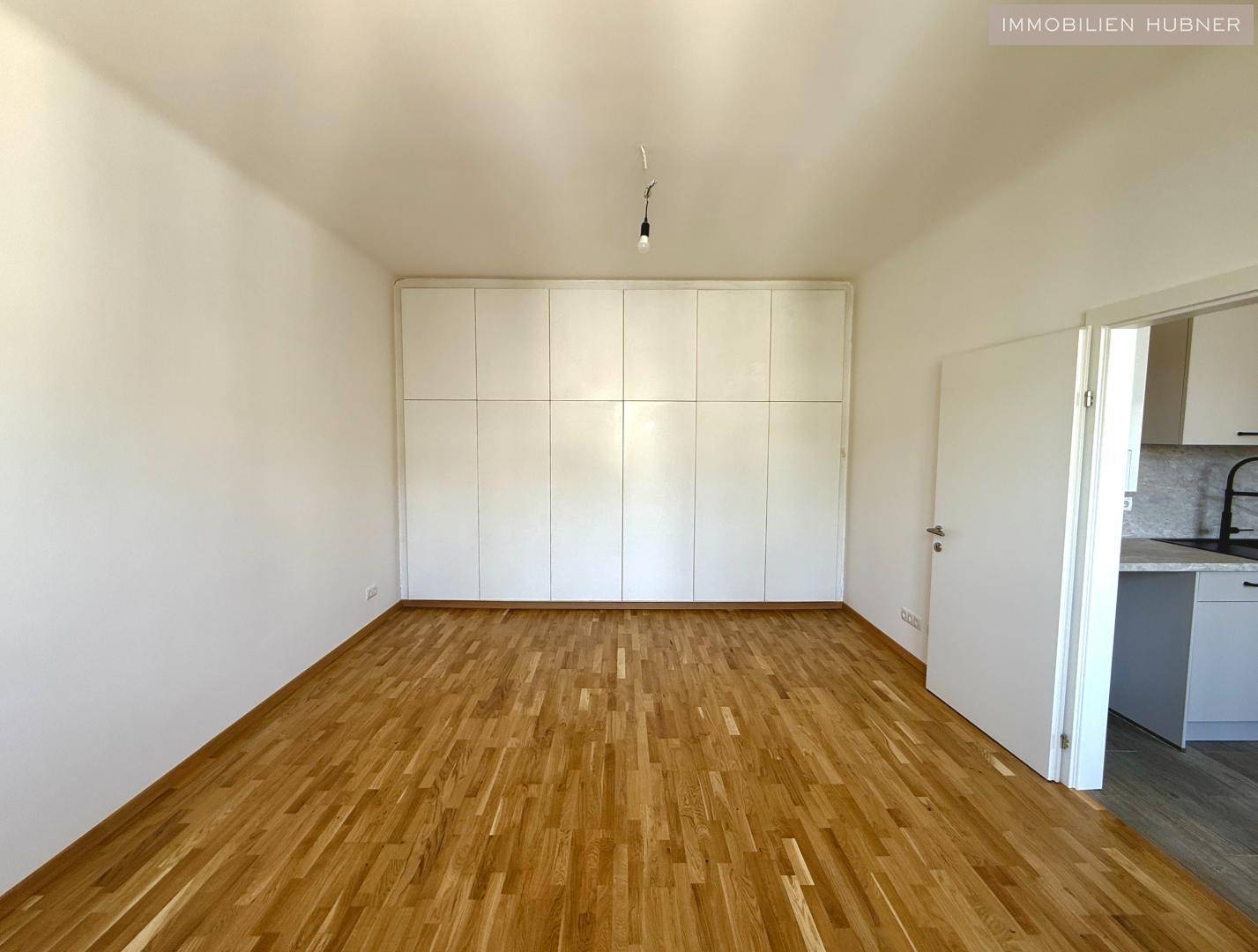 Geräumiges Zimmer mit Holzparkettboden und einem großen, wandhohen Einbauschrank.