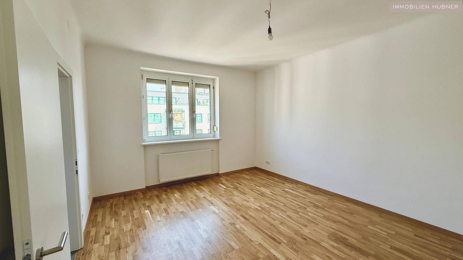 Heller Raum mit Holzparkettboden und einem Fenster, das Tageslicht hereinlässt.