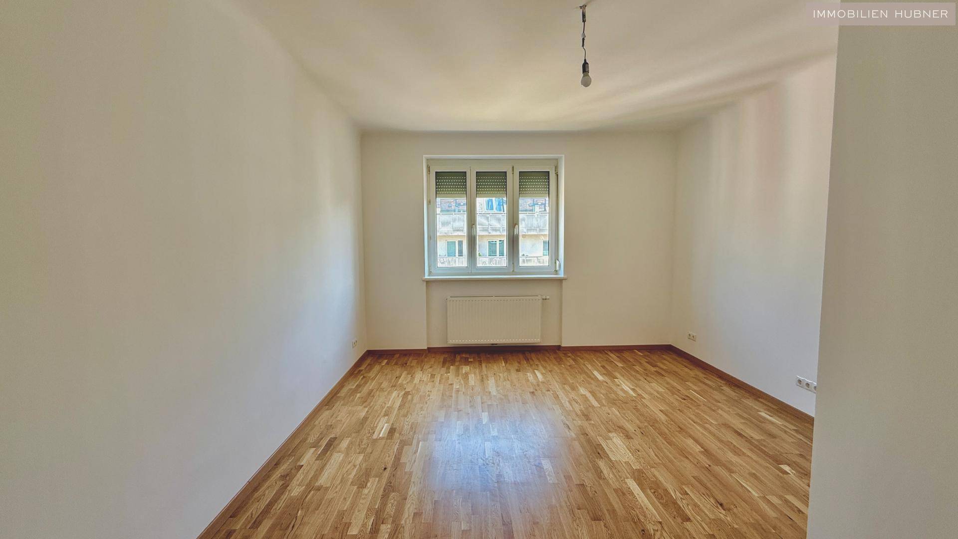 Leeres Zimmer mit schönem Holzparkettboden und einem Fenster mit Jalousien.