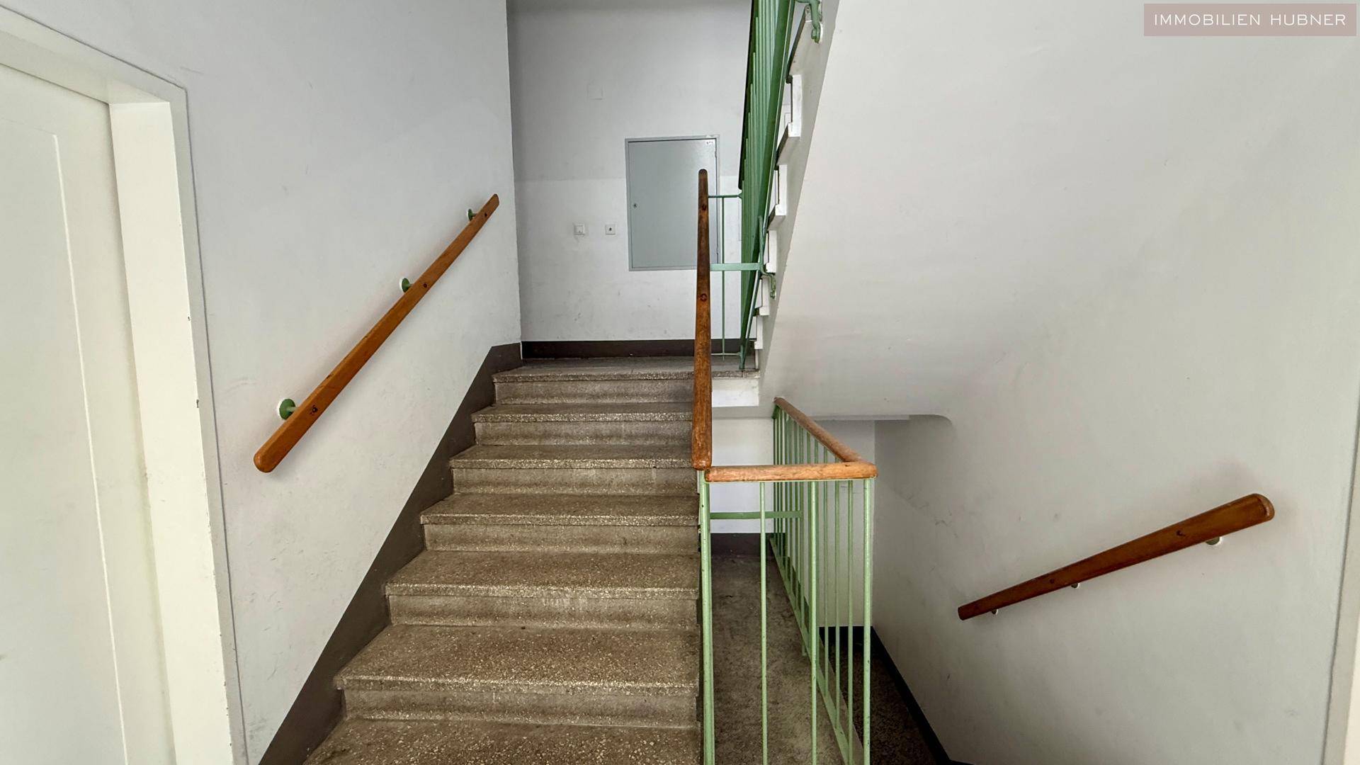 Treppenhaus mit Steinstufen und grünem Geländer, das die verschiedenen Etagen verbindet.