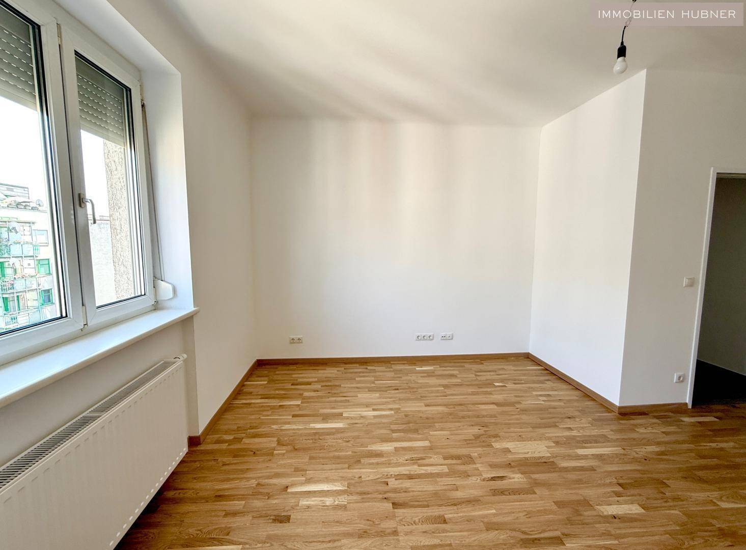 Heller Raum mit Holzparkettboden und einem großen Fenster, das viel Licht spendet.