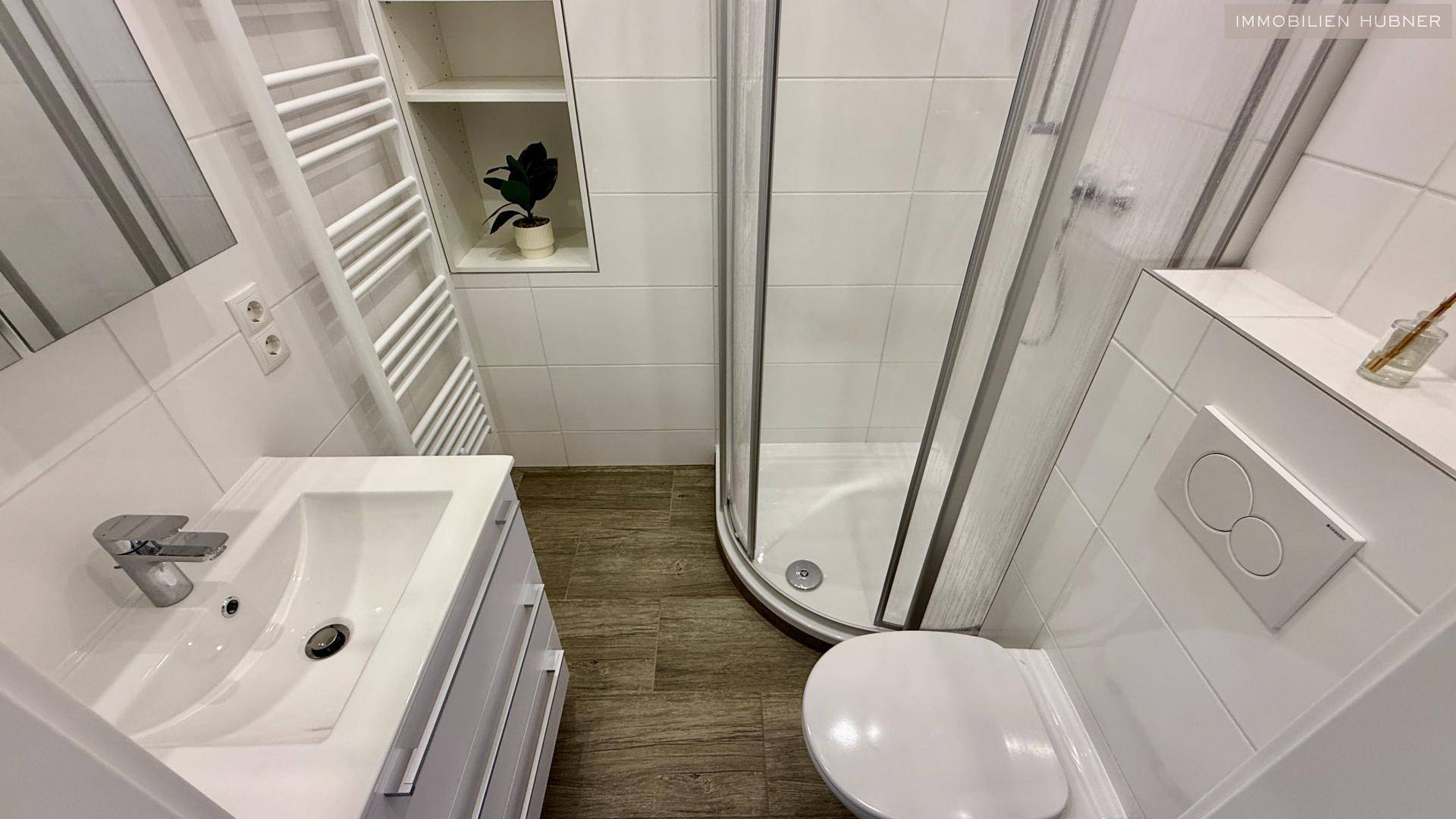Modernes Badezimmer mit weißen Fliesen, Duschkabine, WC, Waschbecken und beheiztem Handtuchhalter.