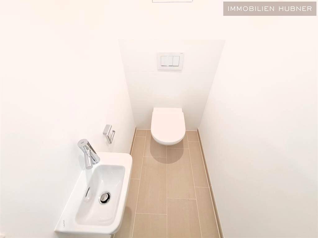 Kleines Gäste-WC mit wandhängendem WC, kleinem Waschbecken und hellen Fliesen.