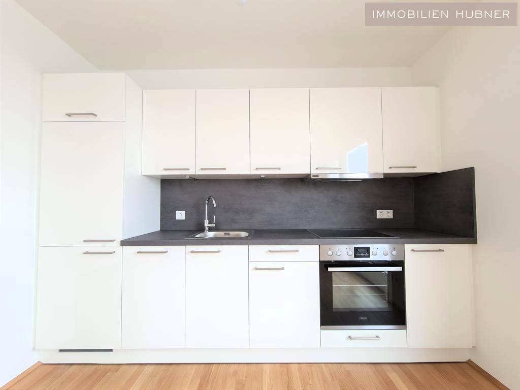 Moderne Einbauküche mit weißen Hochglanzfronten, dunkler Arbeitsplatte und integrierten Geräten.