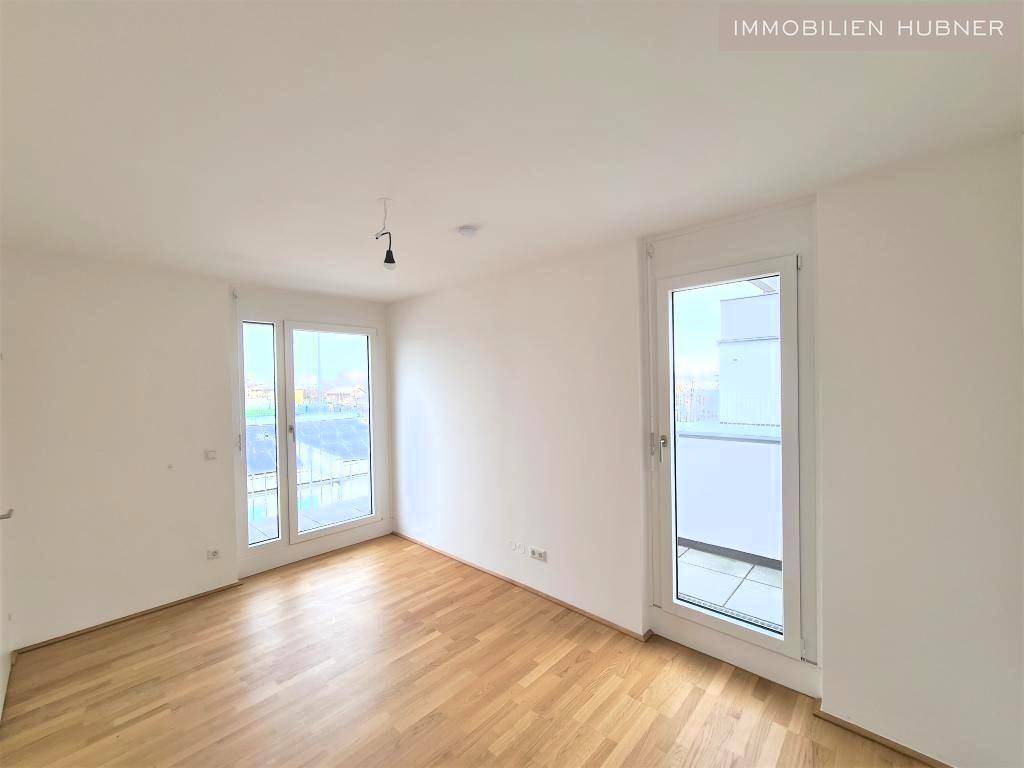 Leeres Zimmer mit hellem Parkettboden und zwei Fenstertüren zum Balkon.