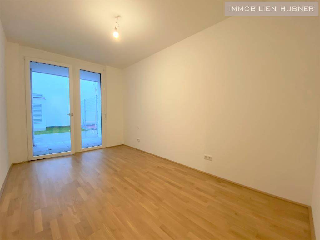 Helles Zimmer mit Holzfußboden und Zugang zu einem Außenbereich.