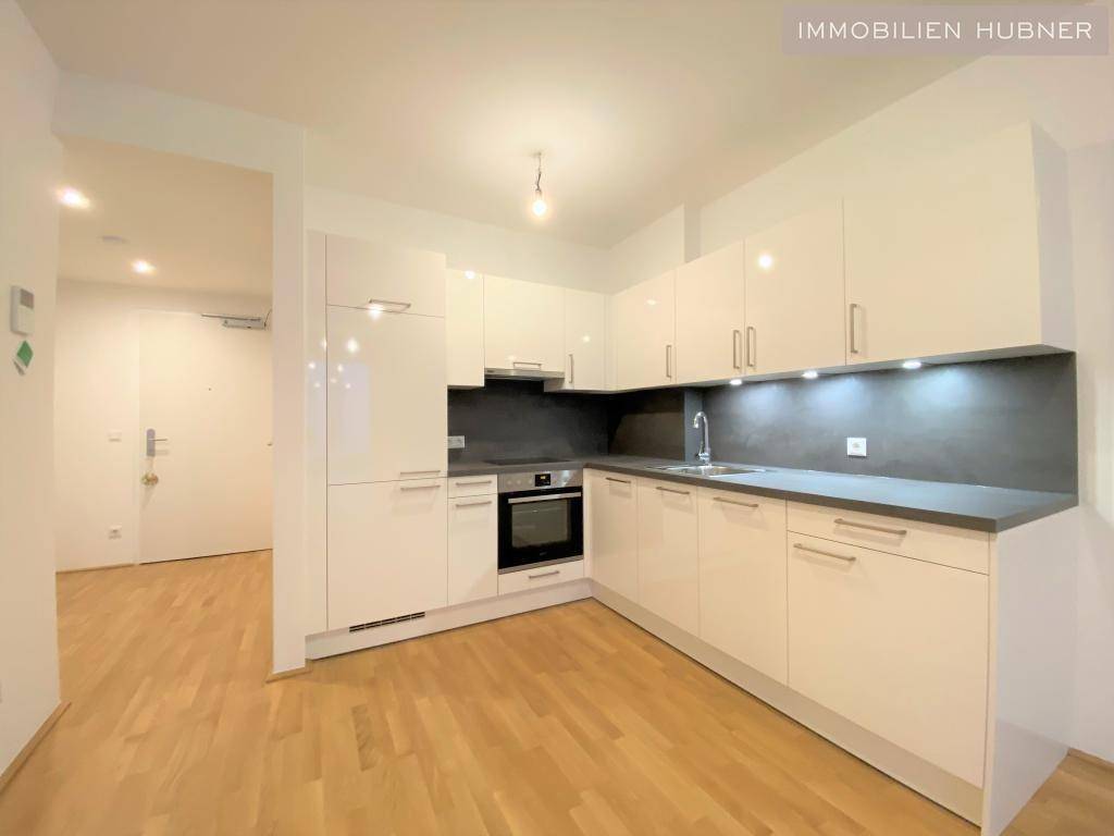 Moderne Küche mit weißen Hochglanzfronten, dunkler Arbeitsplatte und Holzfußboden.