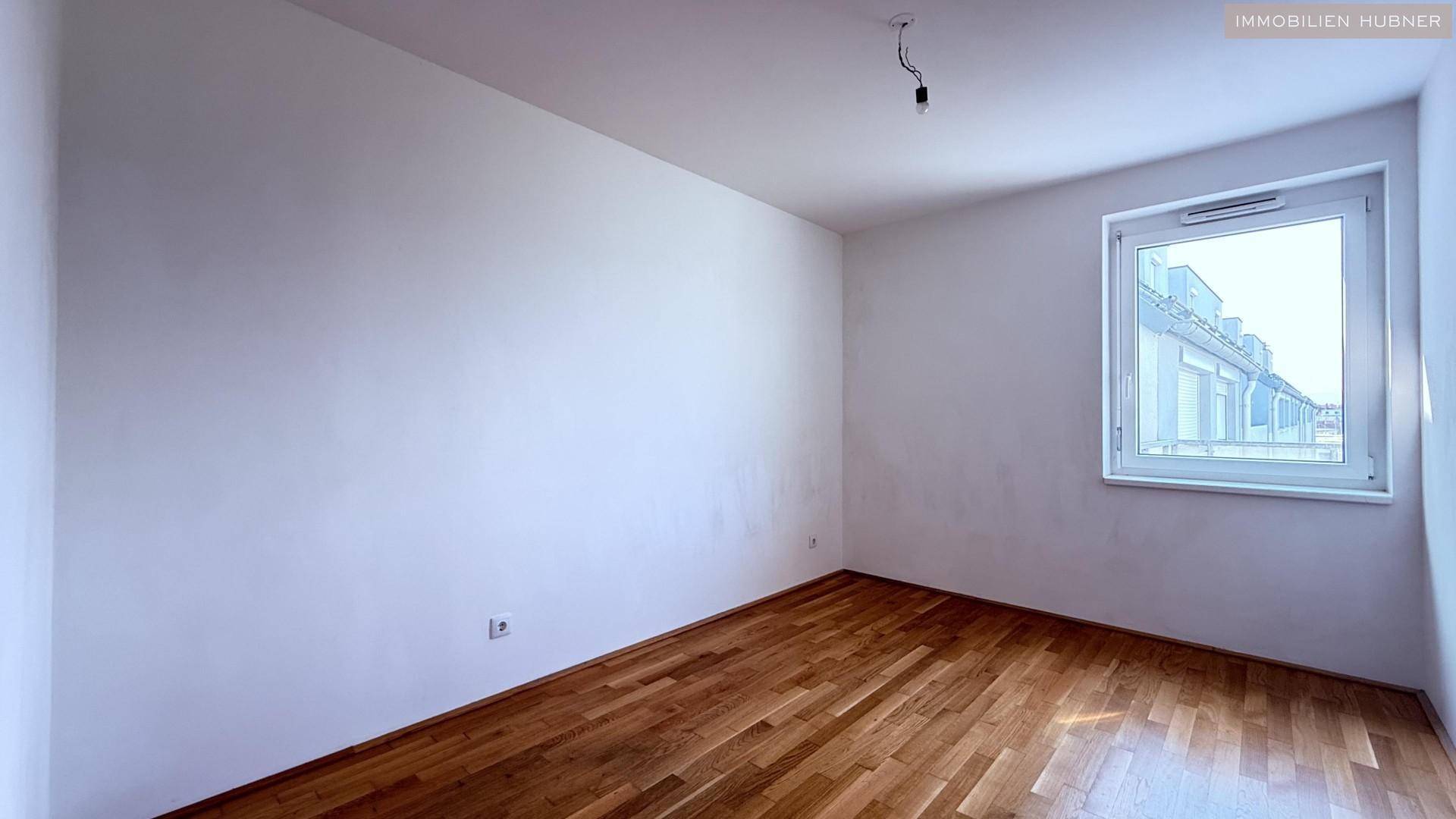 Leeres Zimmer mit Parkettboden und einem Fenster, das den Blick nach draußen freigibt.