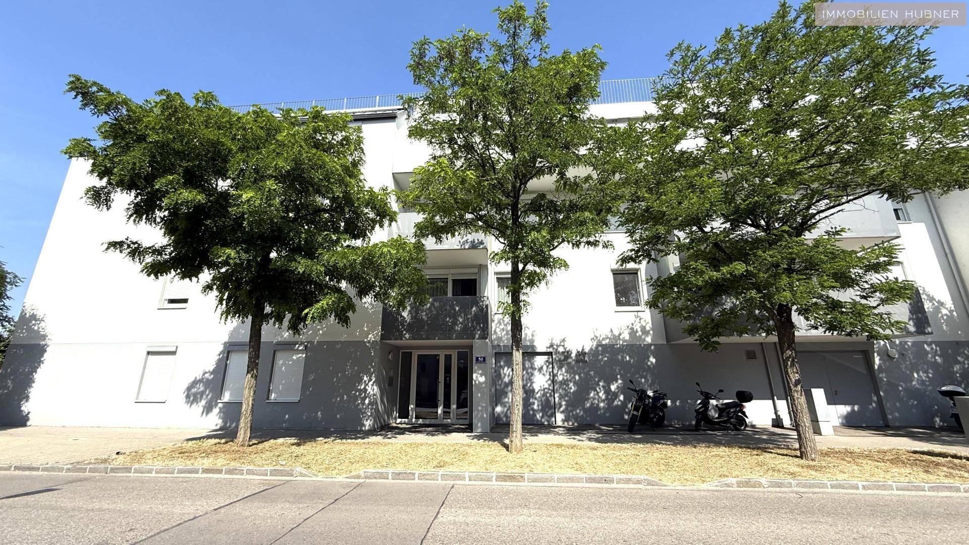 Moderne Wohnhausfassade mit Bäumen davor und Parkmöglichkeiten an der Straße.