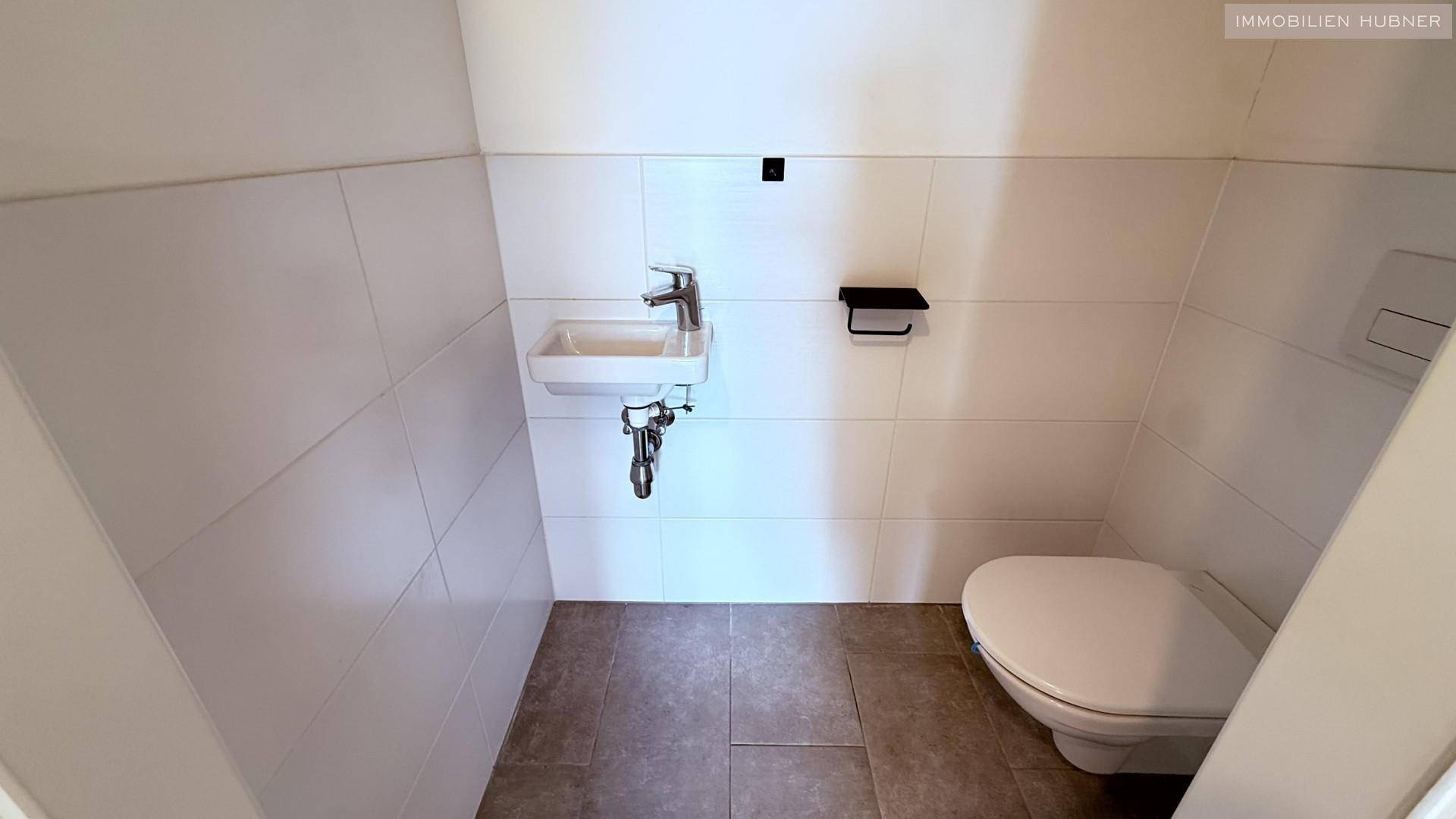 Separates Gäste-WC mit wandhängender Toilette und kleinem Handwaschbecken.