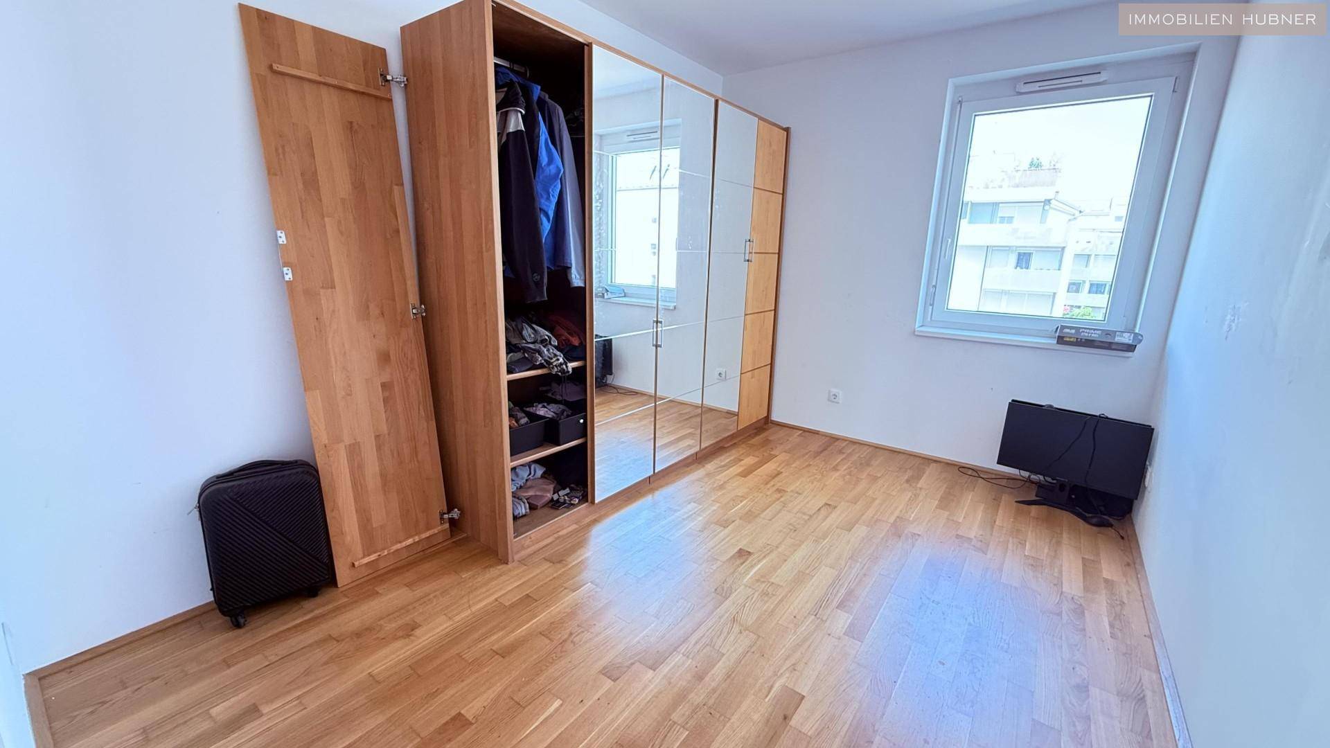 Schlafzimmer mit Spiegelschrank, Holzboden und hellem Fenster.