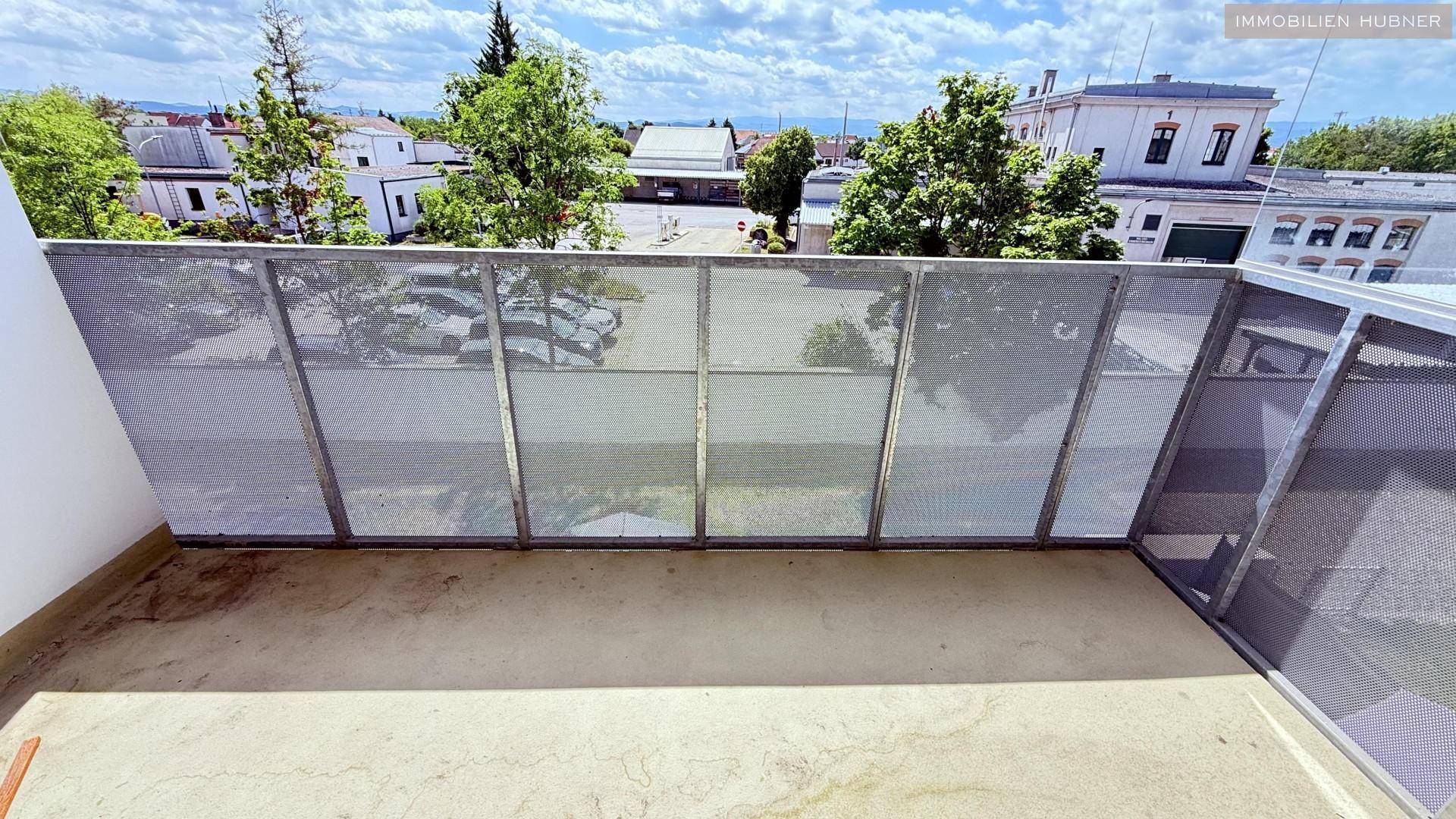 Geräumiger Balkon mit Metallgeländer und Blick auf die umliegenden Gebäude und Bäume.