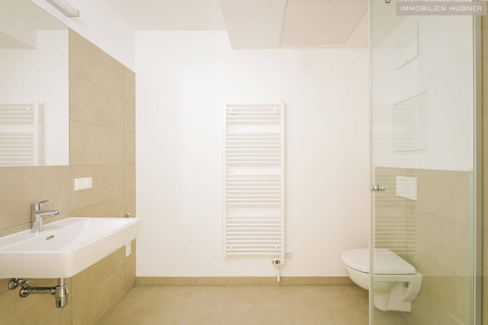 Modernes Badezimmer mit beigefarbenen Fliesen, wandhängendem WC und Duschkabine.