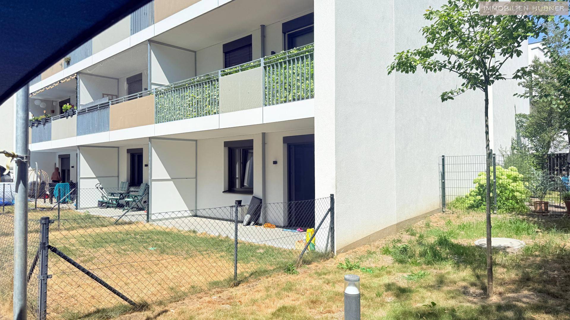 Außenansicht eines Mehrfamilienhauses mit Erdgeschoss-Terrassen und Balkonen im Obergeschoss.