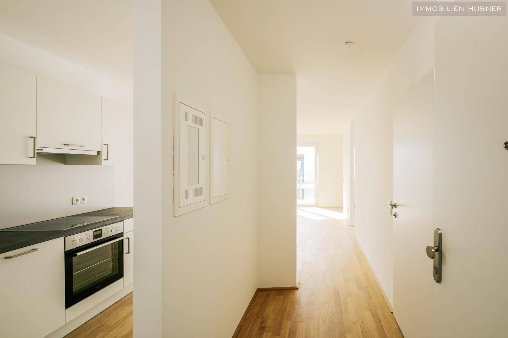 Heller Flur mit Holzboden und Blick in den Wohnbereich sowie eine moderne Küche.