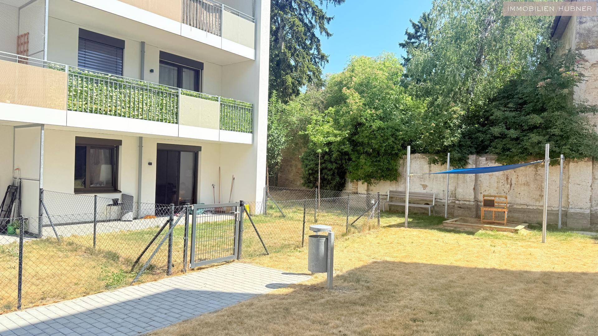 Gartenbereich vor einem Wohngebäude mit Zaun und einfacher Gestaltung.