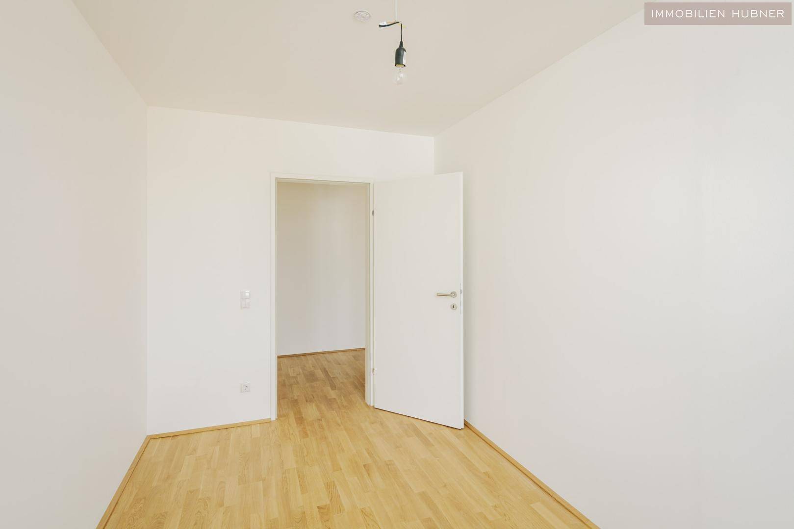 Leeres Zimmer mit Parkettboden und weiß gestrichenen Wänden, bereit zur individuellen Gestaltung.