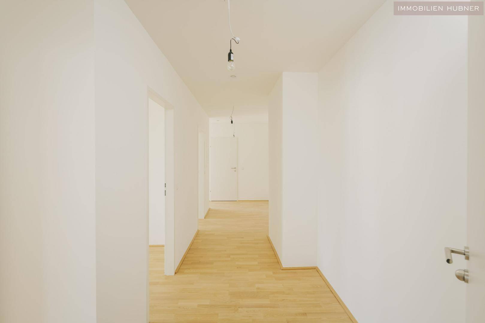Heller Flur mit Parkettboden und weißen Wänden, der zu weiteren Räumen führt.