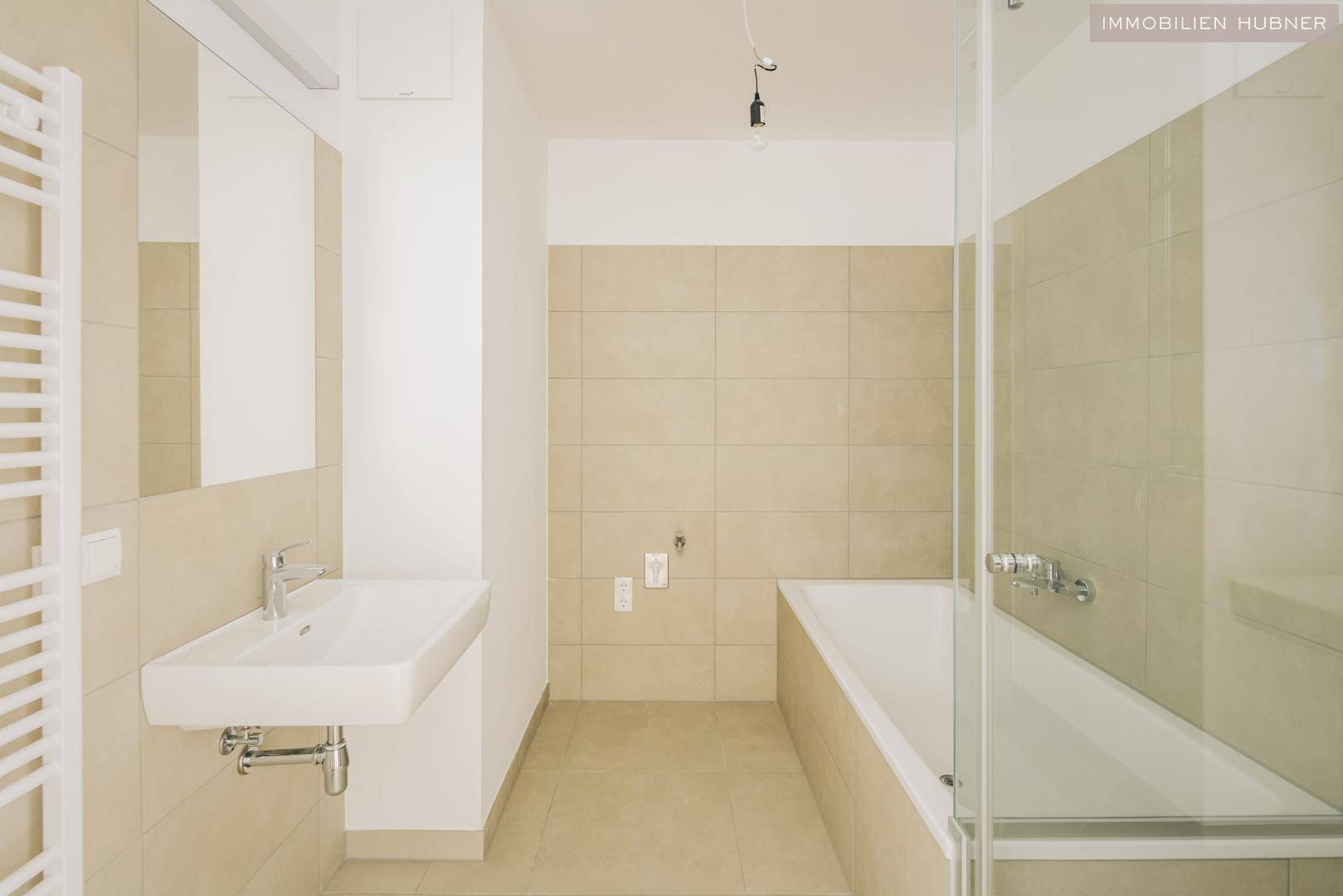 Modernes Badezimmer mit beigen Fliesen, Badewanne und separater Dusche sowie einem Waschbecken.