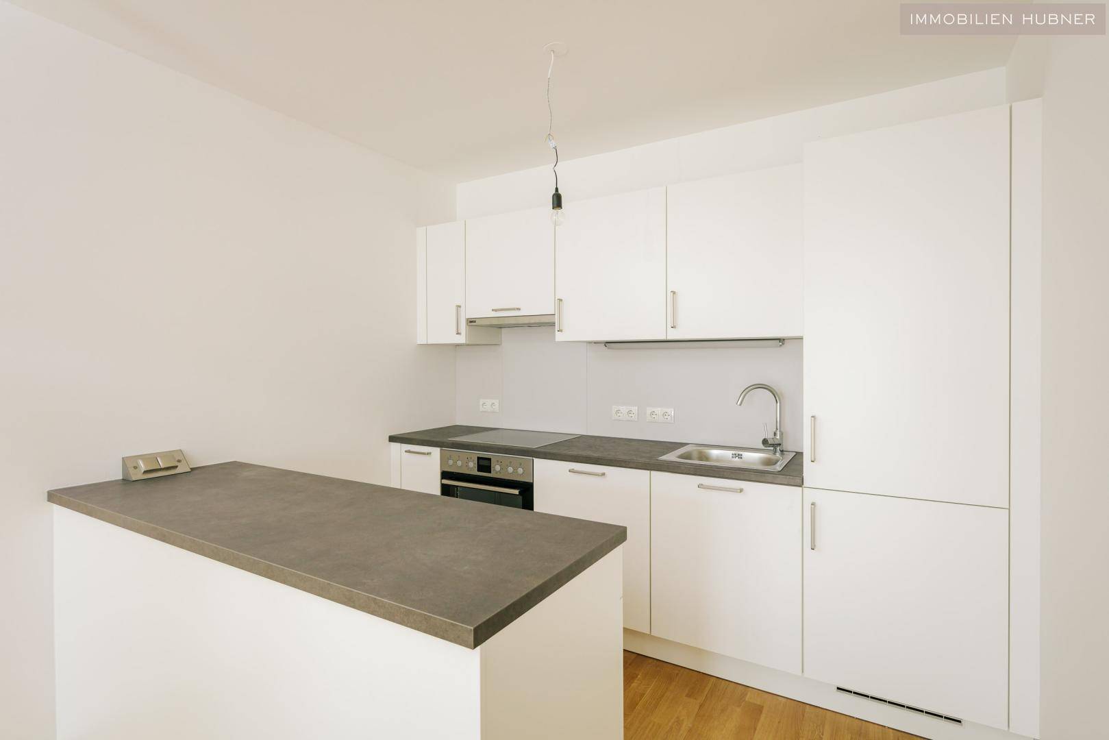 Moderne Einbauküche mit weißen Schränken, grauer Arbeitsplatte und integrierten Geräten.